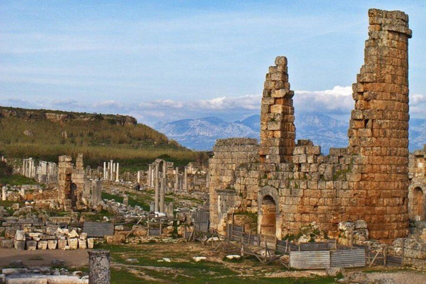 Ancient ruins with stone columns and walls, set against a mountainous backdrop. 1