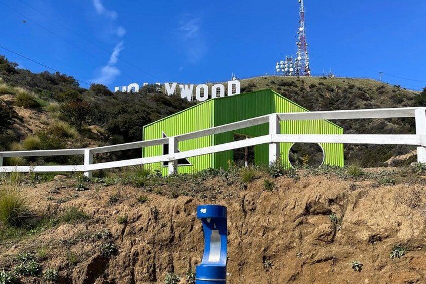 A green building with a white fence in front, a hill with sparse vegetation, and a tall communication tower in the background. 5
