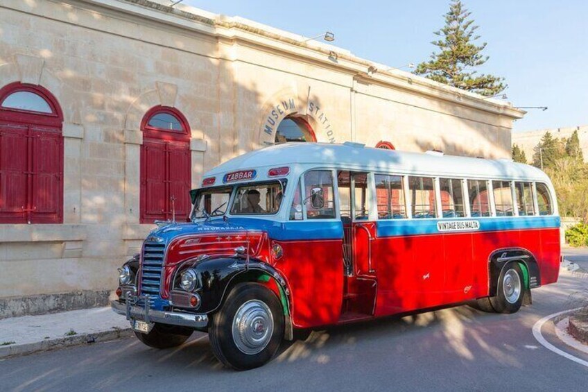 A vintage red and blue bus parked in front of a building with red shutters. 4