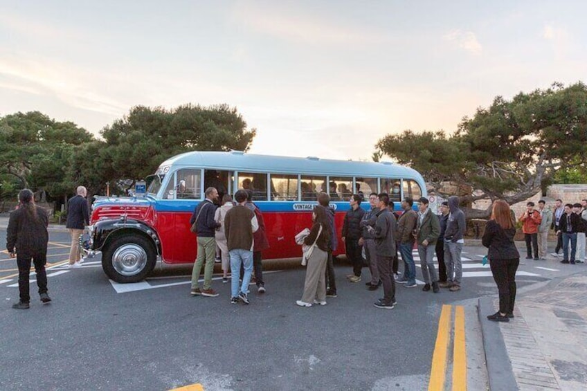 A vintage red and blue bus parked on a street with people standing around it. 1