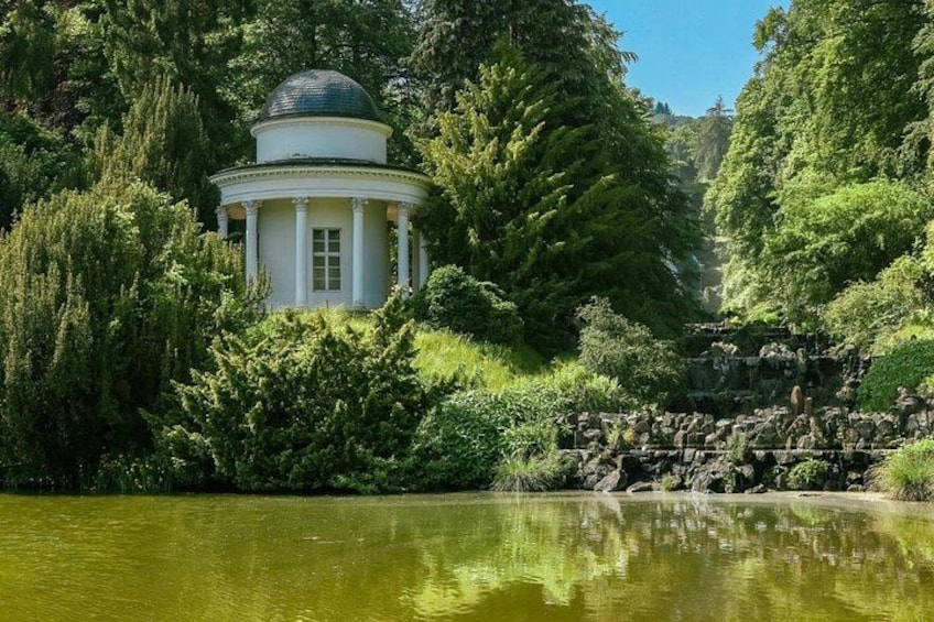 En hvid pavillon med kuppel, omgivet af frodig vegetation og stille vand. 2