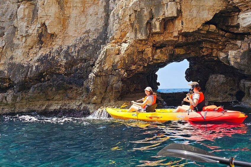 Deux personnes pratiquent le kayak dans une crique rocheuse, d’où la mer est visible en toute clarté. 1