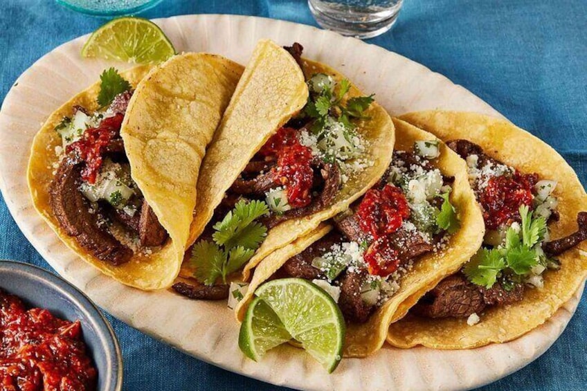 Three tacos with meat, cilantro, and a lime wedge on a plate. 1