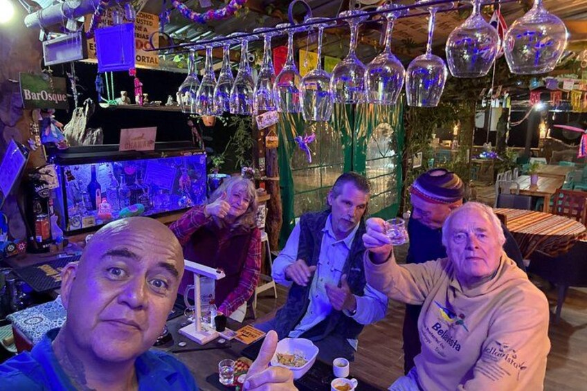 A group of people sitting at a table with drinks, surrounded by hanging glassware and a bar area. 3