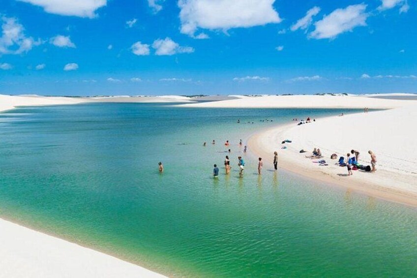 A beach with clear turquoise water, people swimming and sunbathing, and white sand dunes in the background. 2