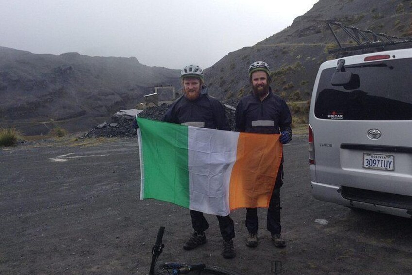 Two people holding a flag, a van, and a rugged landscape. 2