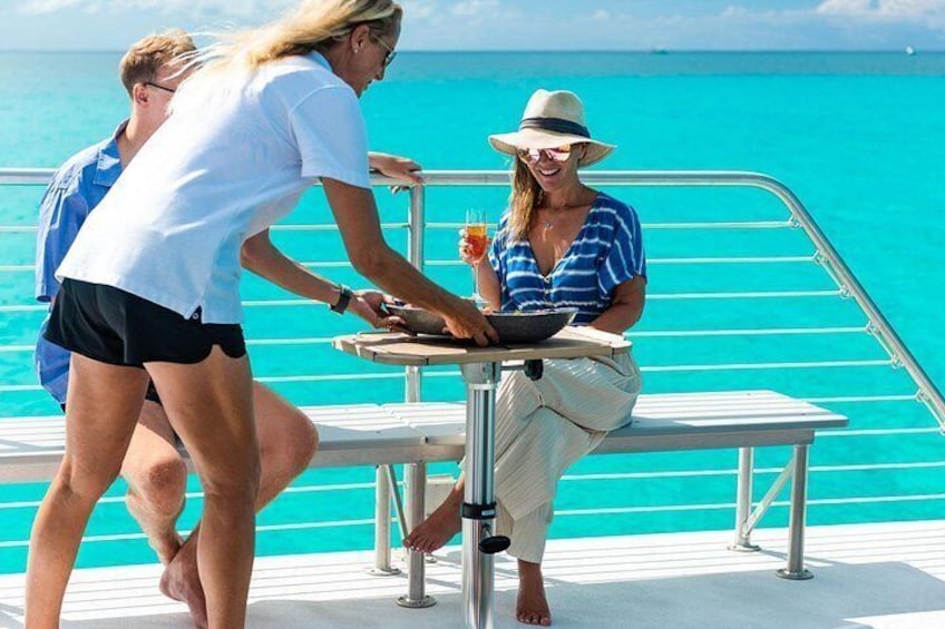 Una persona sentada a una mesa en un barco, con agua turquesa al fondo. 2