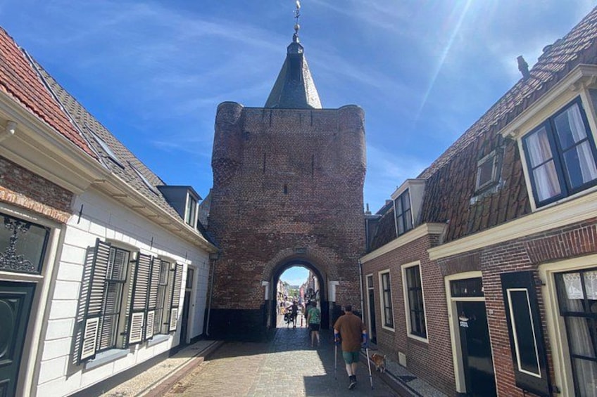A narrow street with a brick tower, white buildings with shutters, and a clear blue sky. 3
