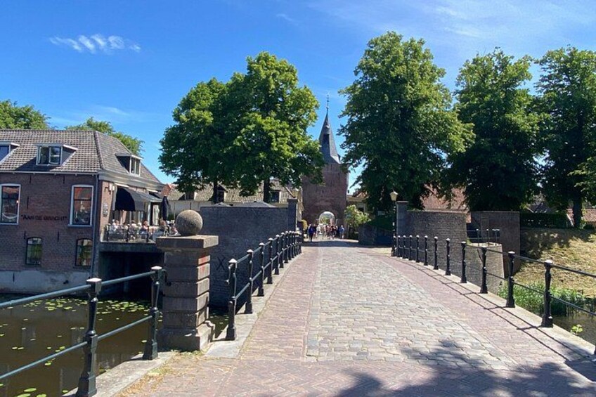 A cobblestone bridge with a railing, a church steeple in the background, and a building with a sign on the left. 5