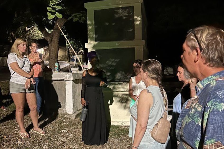 A group of people standing outdoors, some holding drinks, near a concrete structure with a cross on top. 4