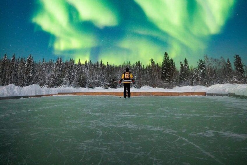 A person on an ice rink with the Northern Lights in the background. 2