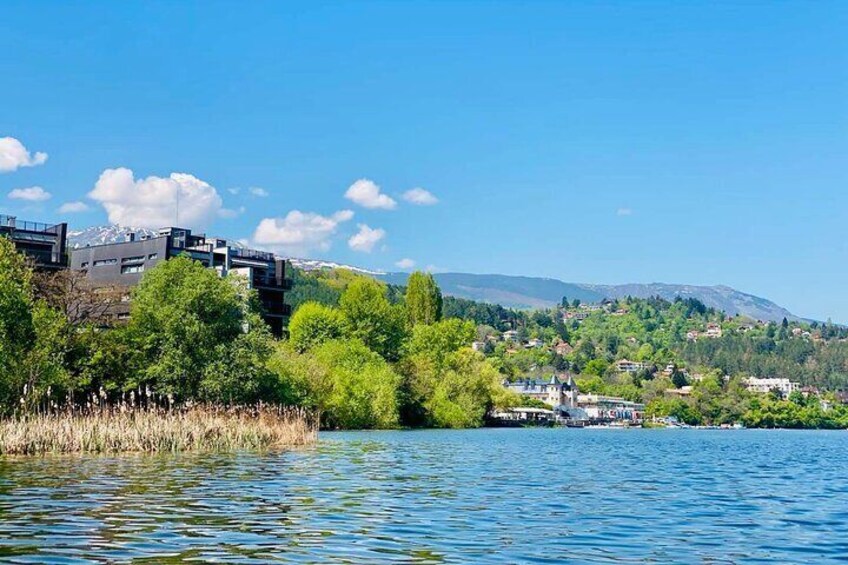 A lake with buildings on the left and a hilly landscape in the background. 1
