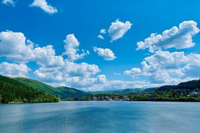 A calm lake surrounded by green hills under a blue sky with scattered clouds. 5