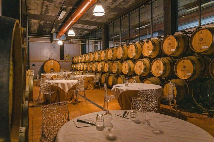 A wine cellar with rows of wooden barrels and tables set up for tasting. 5