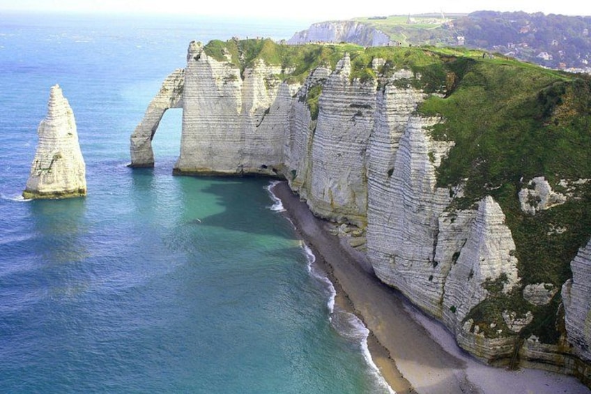 A coastal landscape with white chalk cliffs, a narrow beach, and a clear blue sea. 1
