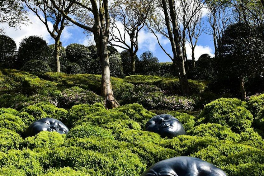 A landscaped garden with manicured bushes, a large tree, and a black spherical sculpture. 5