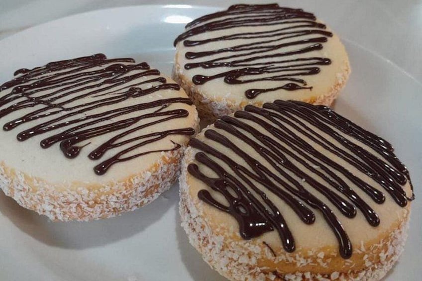 Tre ciambelle intinte nel cioccolato, con glassa bianca e scaglie di cocco su un piatto bianco. 2