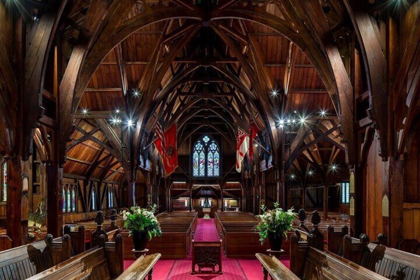 A church interior with wooden pews, a central aisle, stained glass windows, and flags. 5