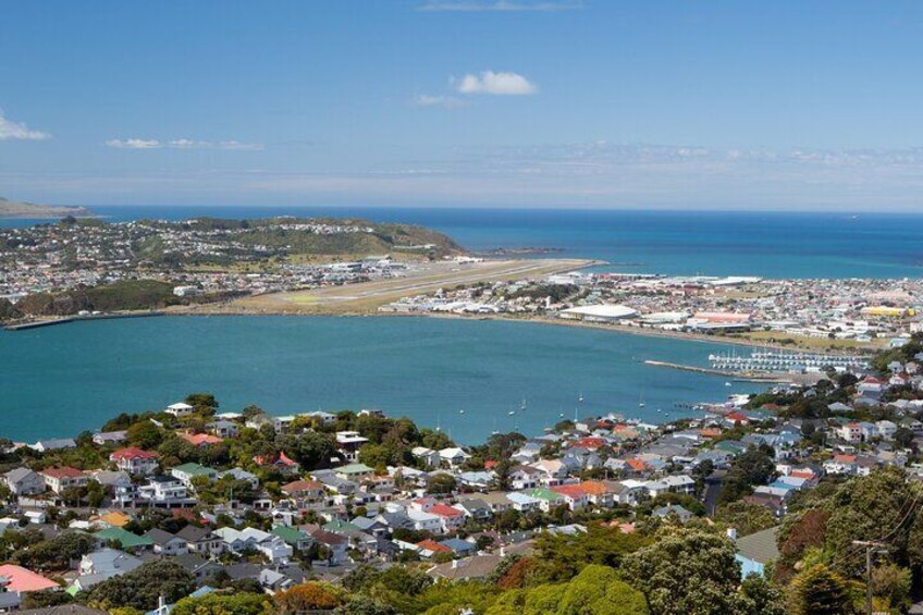A coastal town with houses, a marina, and a view of the ocean and distant city. 4