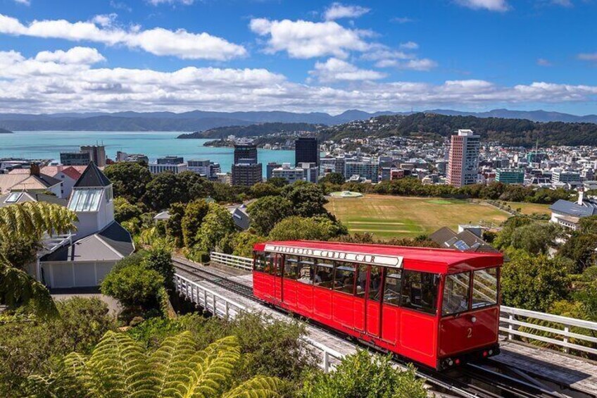 A red cable car moving along a track with a cityscape and mountains in the background. 1