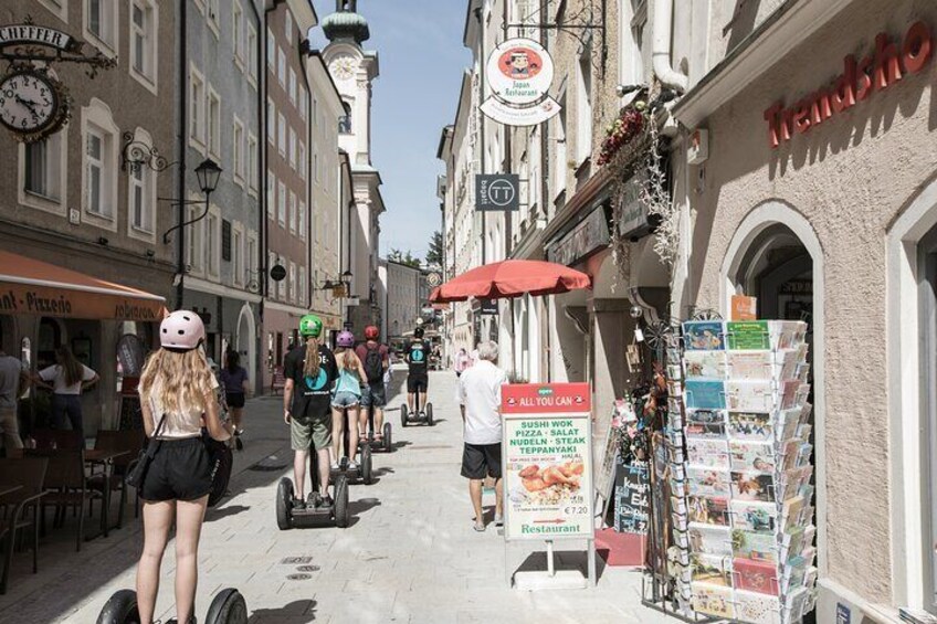 A street with people riding scooters, a sign for a restaurant, and a shop selling magazines. 5