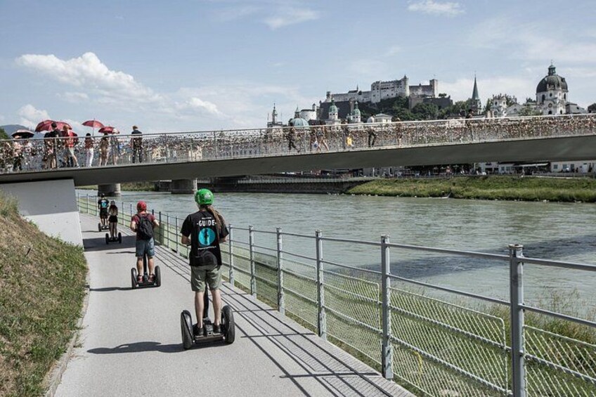 A river with a bridge, people on segways, and a cityscape in the background. 2