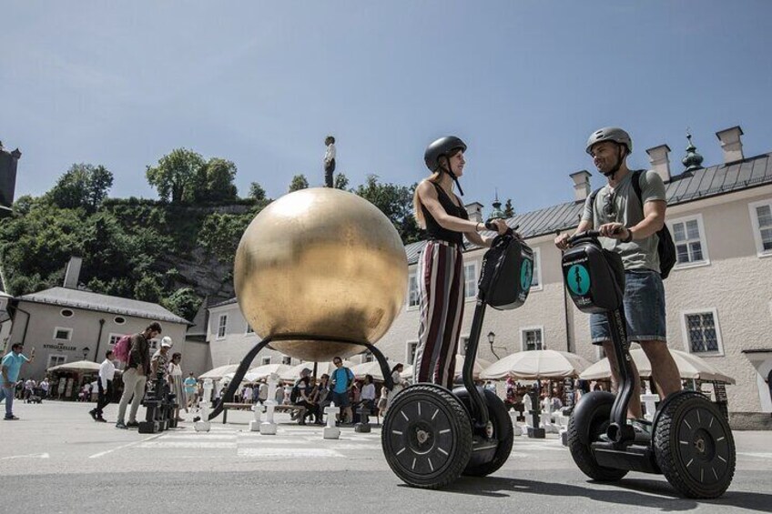 Two people riding Segways on a street with a large golden sphere sculpture in the background. 4