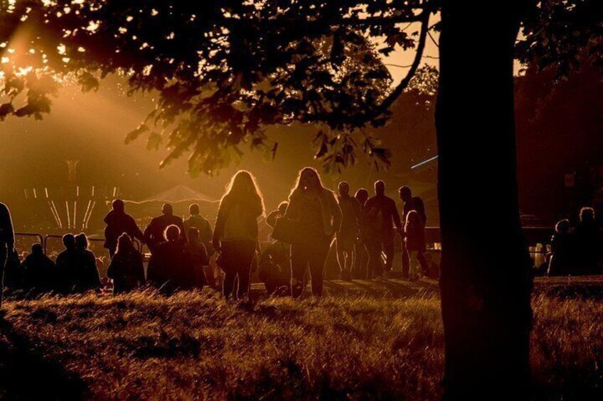 Un grupo de personas reunidas en un campo cubierto de hierba, con árboles y un atardecer al fondo. 2