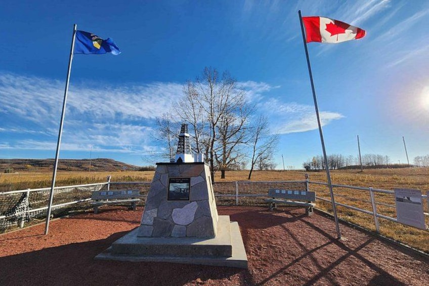 A monument with a plaque, two flags, a bench, and a fenced area. 5