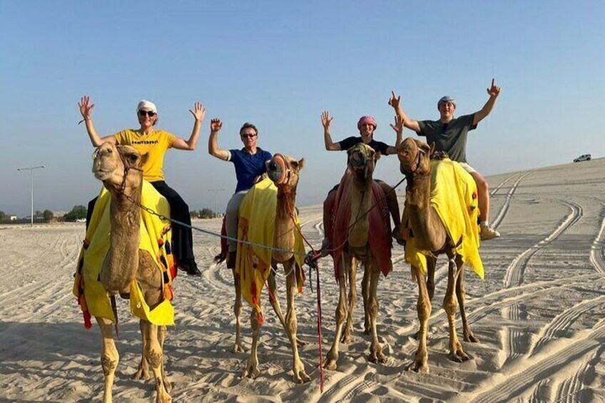 Un grupo de personas montando camellos sobre terreno arenoso, con surcos de neumáticos. 4