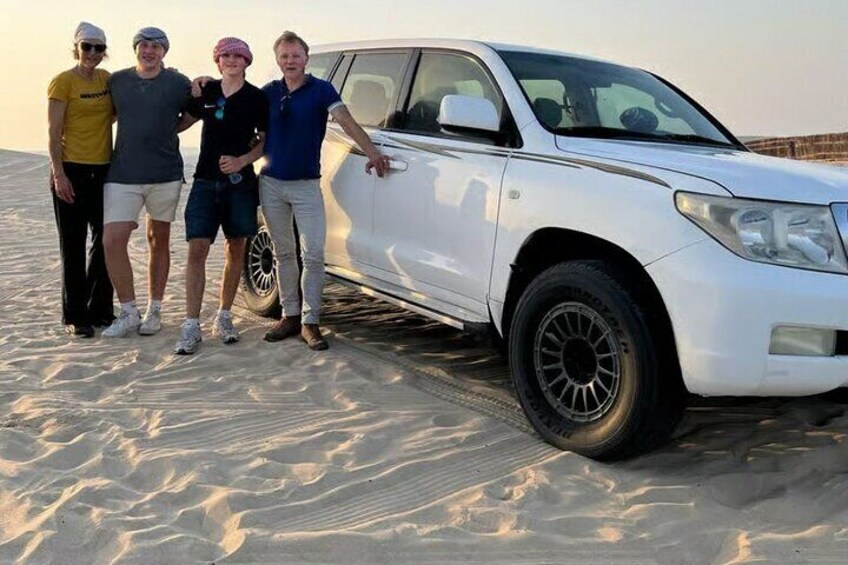 Un SUV blanco estacionado en una playa arenosa, con cuatro personas de pie a su lado. 3