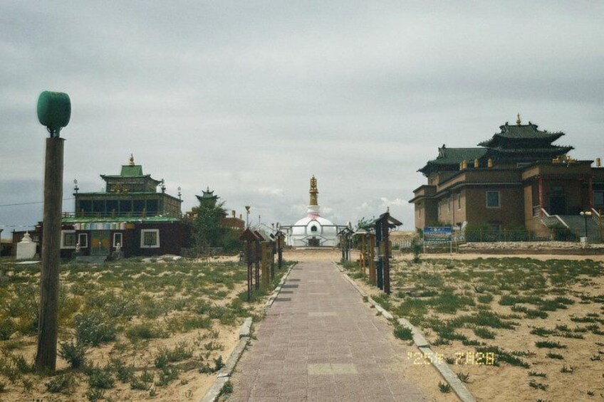A pathway leading to a white building with a green roof, flanked by two traditional structures with green roofs. 2