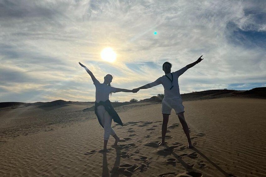 Two people dancing on a sandy beach with the sun in the background. 5