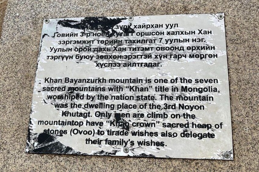 A weathered sign with text in a foreign language and English about Khan Bayanzurkh mountain. 4