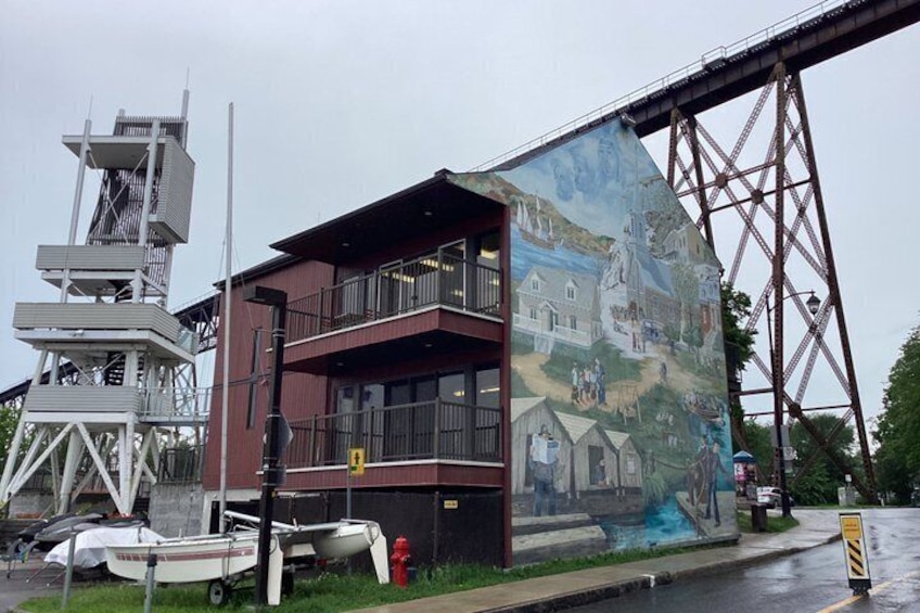 Un edificio con un mural, un hidrante rojo y un puente al fondo. 3