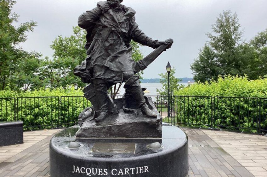 Una estatua de Jacques Cartier sobre un pedestal con una placa, rodeada por un parque con una cerca y árboles. 4