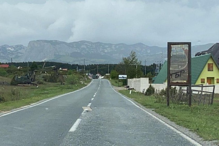 A road with a billboard, a green-roofed building, and mountains in the background. 2