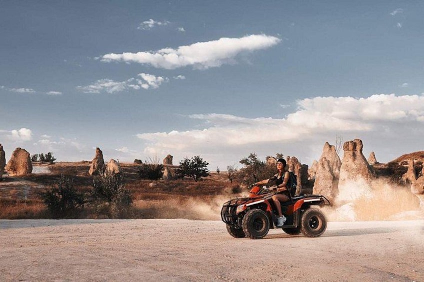 A person riding an ATV on a dirt road with rock formations in the background. 1
