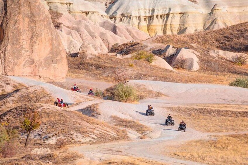 A group of off-road vehicles on a dirt trail in a desert landscape with eroded rock formations. 2