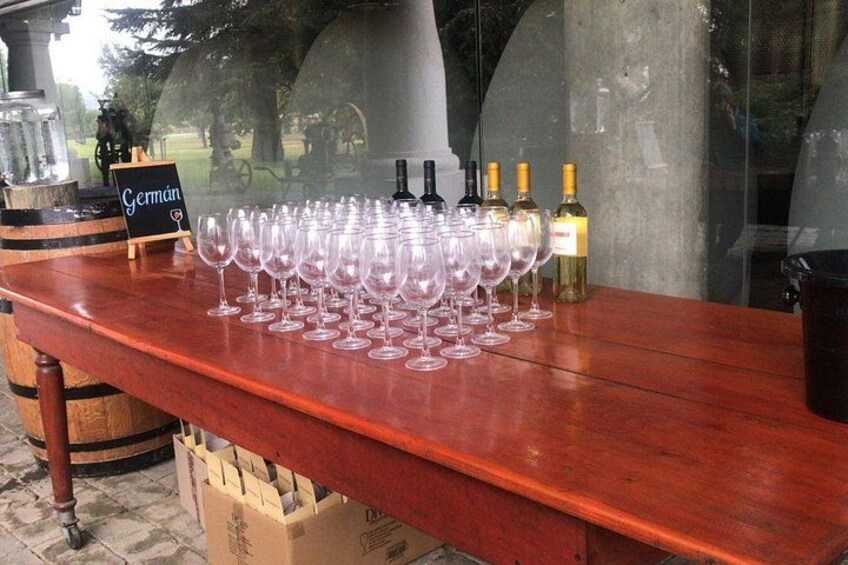 Una mesa de madera con copas y botellas de vino, un letrero de pizarra y un barril. 4