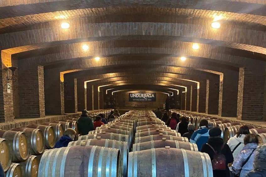 Una bodega con hileras de barricas y gente caminando. 5