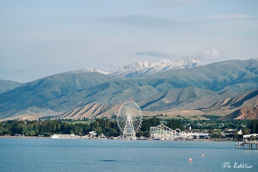 Un lac avec une grande roue, des montagnes et un navire de croisière. 1