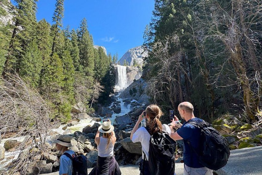 A waterfall surrounded by trees, with people taking photos. 2
