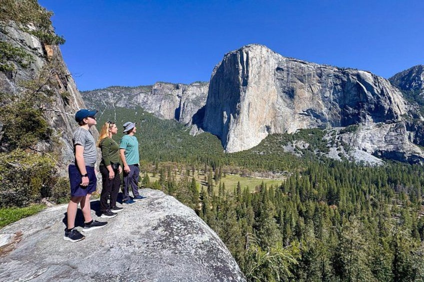 A group of people standing on a ledge overlooking a valley with a prominent rock formation in the background. 4