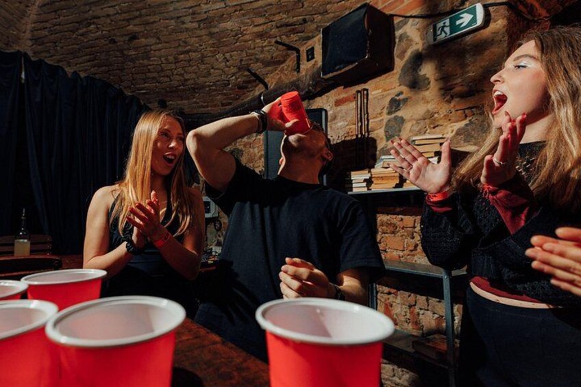 A group of people playing beer pong in a rustic setting with brick walls and wooden tables. 5