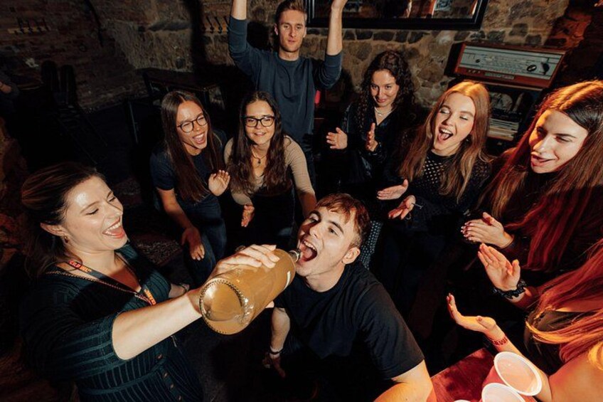 A group of people clapping and cheering in a dimly lit room with stone walls. 1