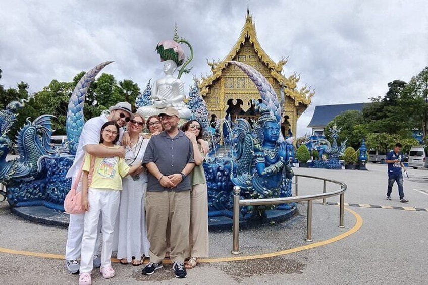 En gruppe mennesker poserer foran en blå og hvid dragefigur med et gyldent tempel i baggrunden. 1