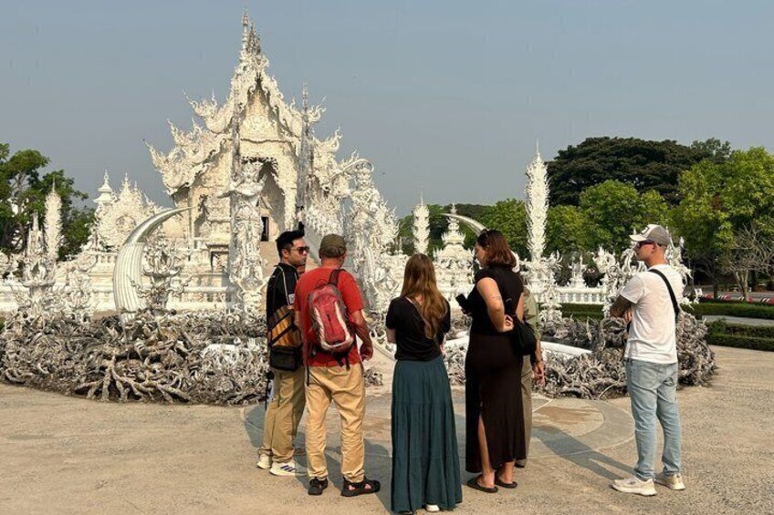 Un gruppo di persone davanti a un tempio bianco, con architettura ornata e dettagliata. 1