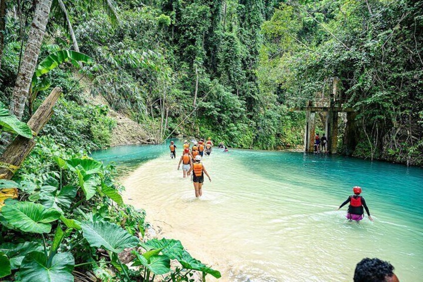 A group of people walking along a riverbank in a tropical forest. 1