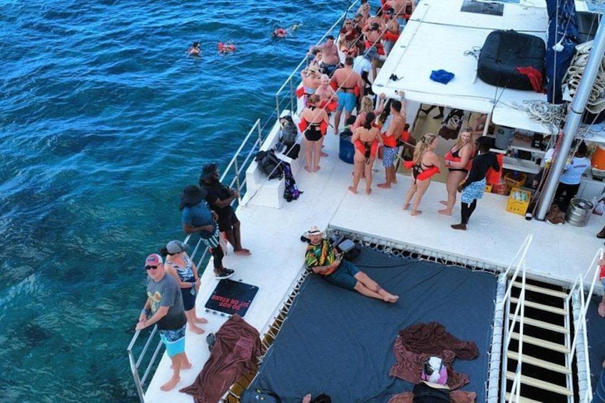 A boat with people standing and sitting on the deck, some in swimwear, and a ladder leading down to the water. 2